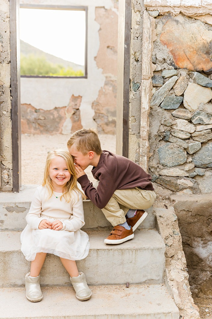 big brother is telling little sister a secret while they sit on old steps in phoenix