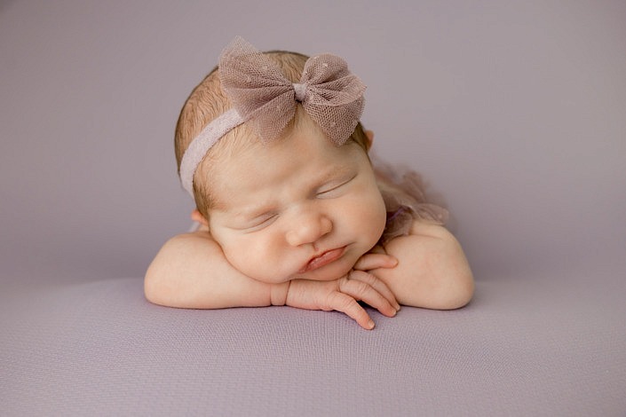 Sleeping newborn girl laying on her hands on a purple background