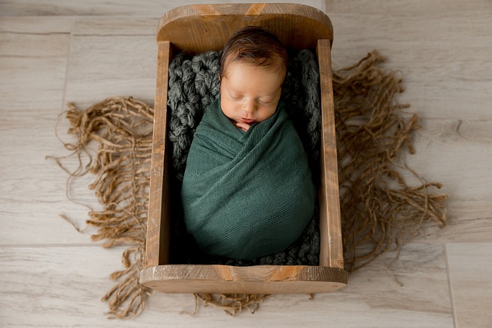 sleeping newborn boy wrapped in a gorgeous green color sleeping in a wood bed