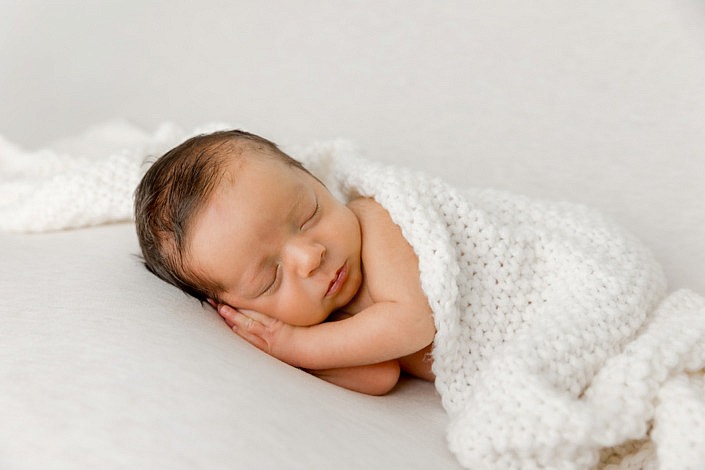 side lying newborn boy sleeping on his hands wrapped in a white knit wrap