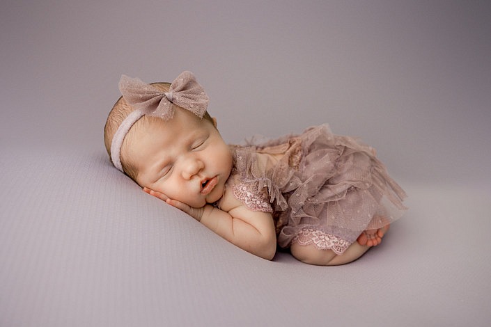 sleeping newborn girl curled up with her ruffle bum in the air against a purple background