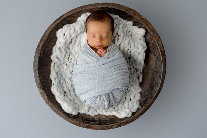 baby boy wrapped in blue laying in a large wood bowl on top of a blue floor