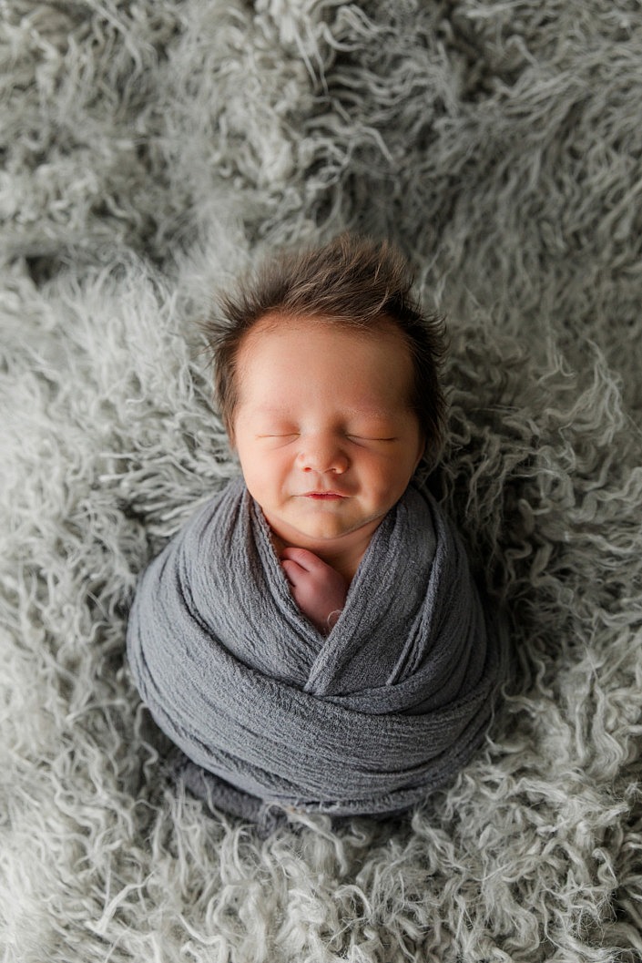smiling and sleeping newborn boy with full head of hair
