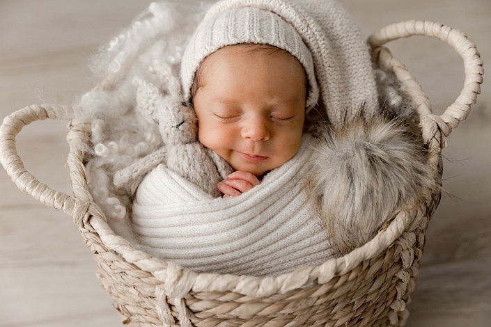 smirking baby boy with a sweater sleepy hat on while cuddling a stuffed bunny