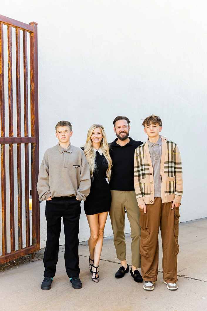well dressed family standing against a white wall with brown gate in scottsdale