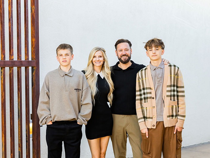 well dressed family standing against a white wall with brown gate in scottsdale