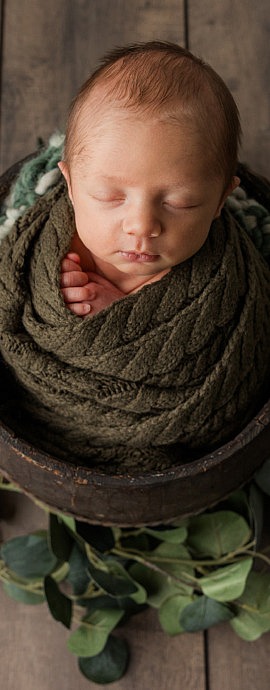 Newborn baby boy in a wood bucket on wood floor