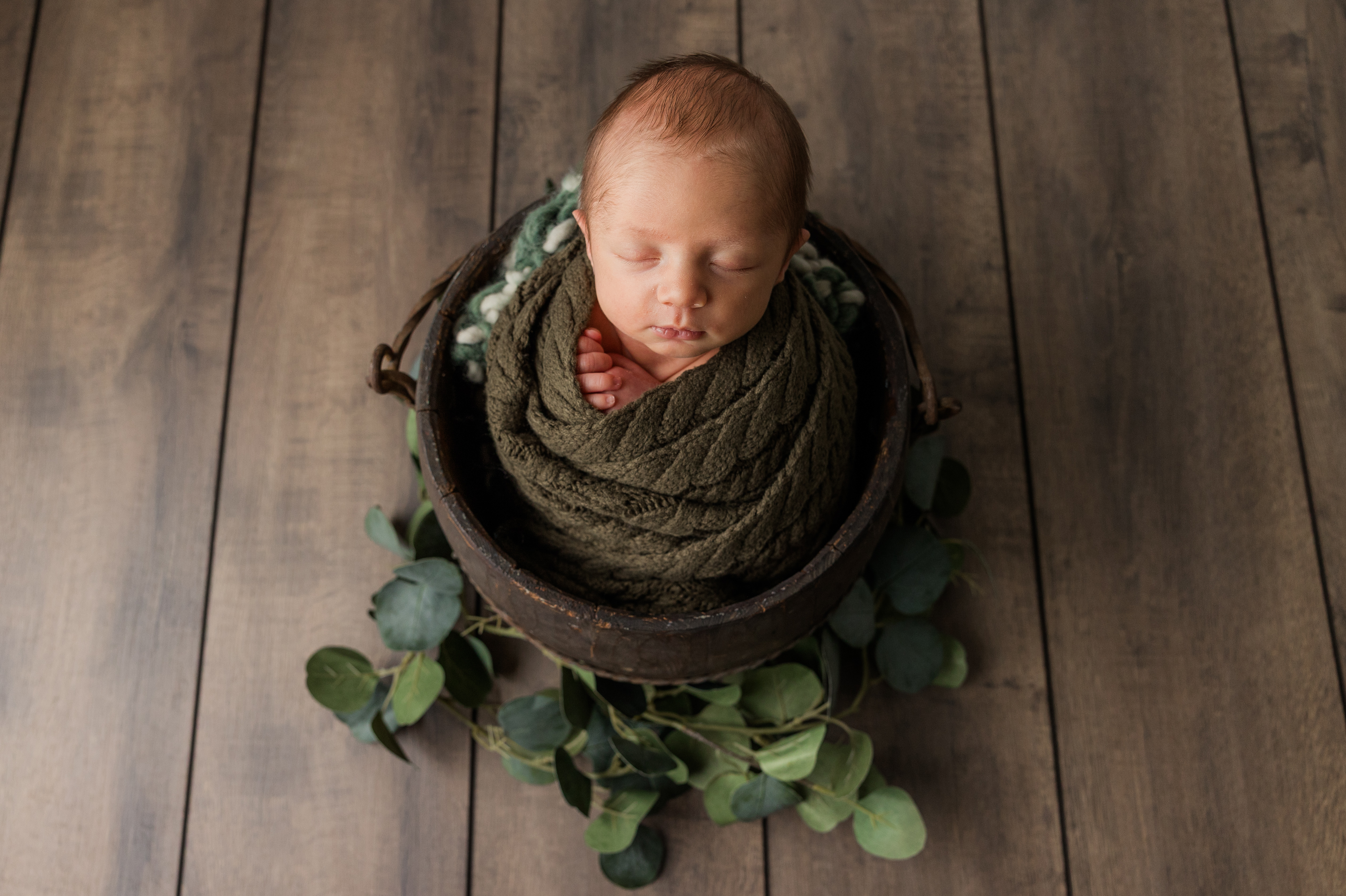 Newborn baby boy in a wood bucket on wood floor