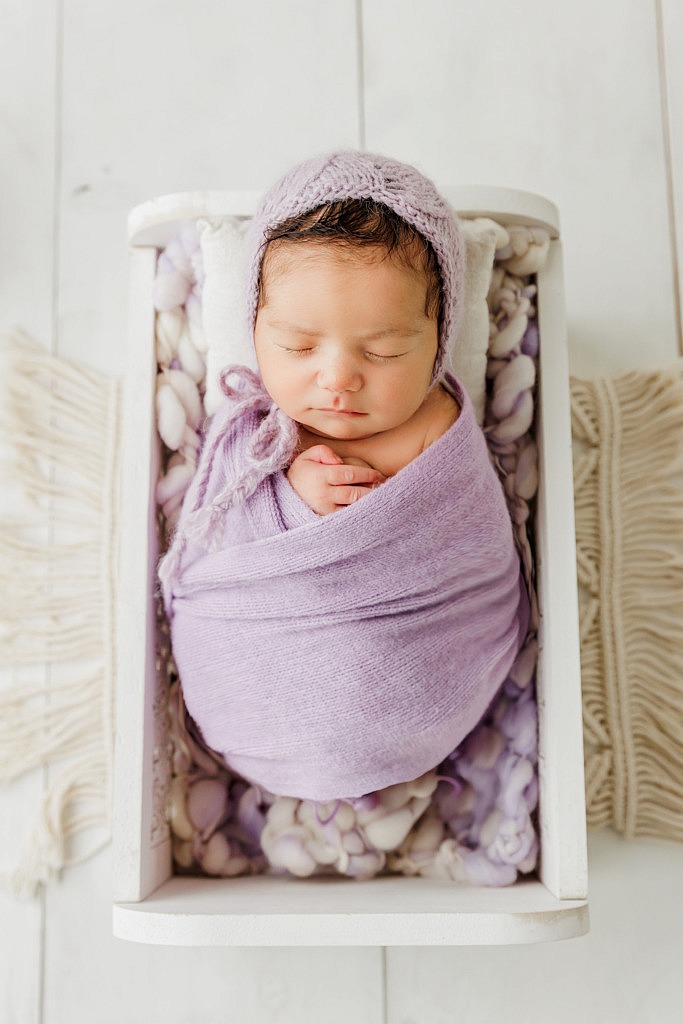newborn girl wrapped in light purple in a little white bed