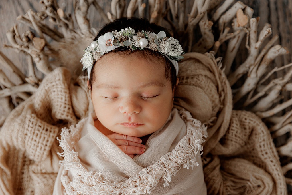 newborn girl wrapped in neutral colors with a floral headband