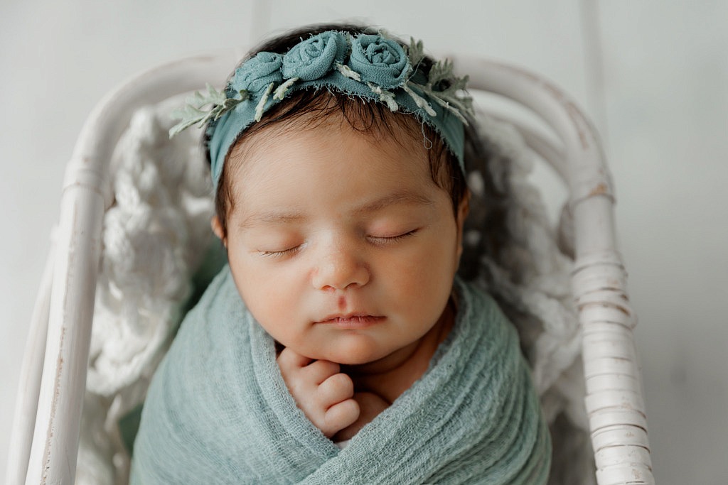 newborn girl wrapped in blue in a white basket