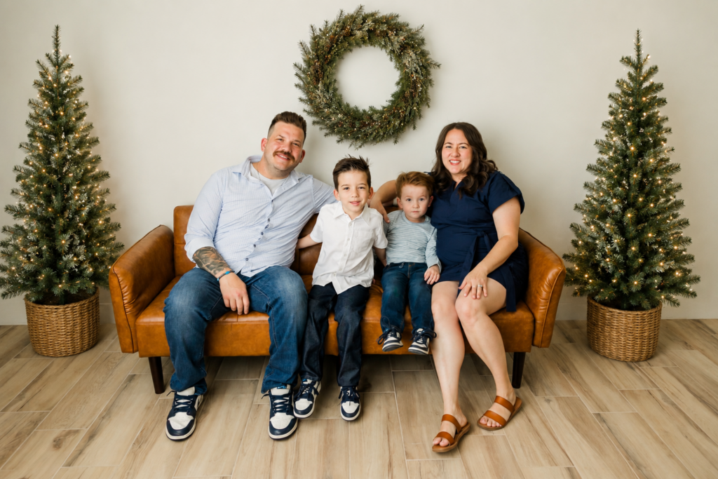 Family sitting on a couch with christmas trees and christmas wreath around them